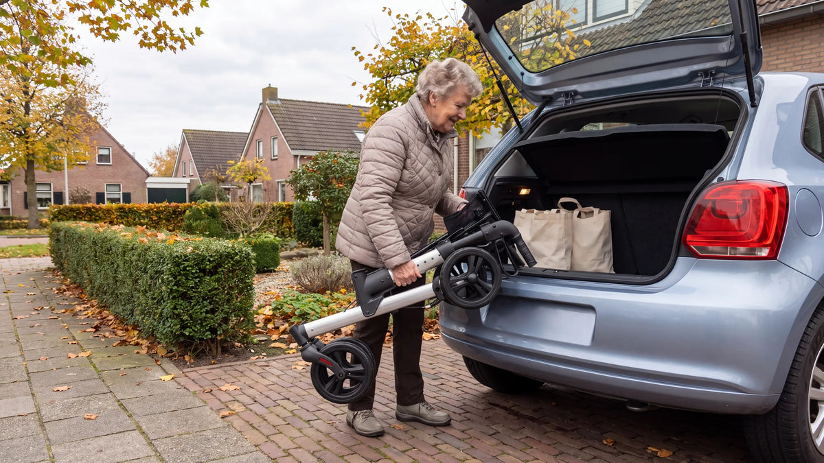 Folded Parvum Riva in gray; a woman lifts it into the trunk of her car on her driveway.
